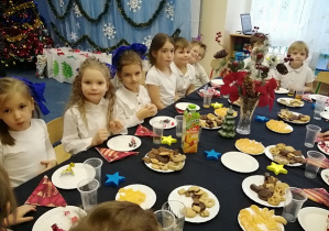 Dzieci siedzą przy stoliku i częstują się słodkimi smakołykami